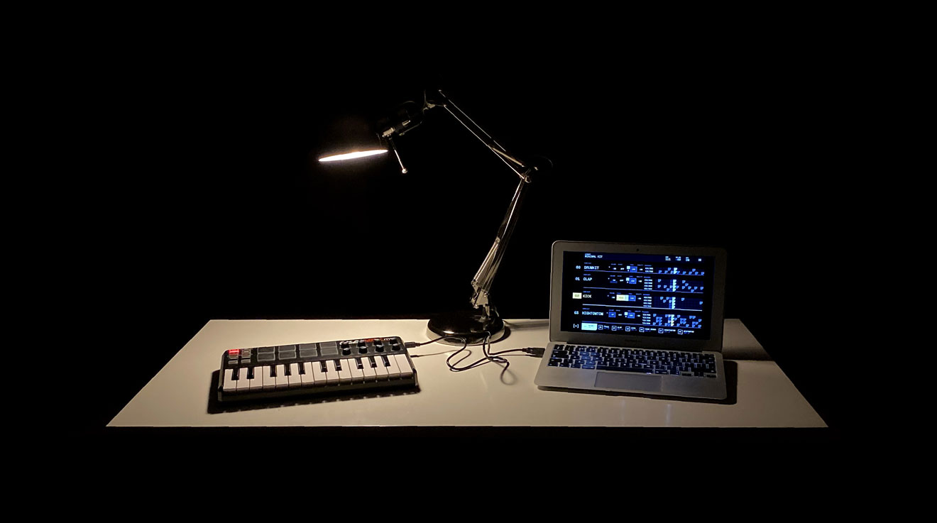 White desk on a pitch-black background, with a lamp and an Akai MPK Mini connected to a laptop showing the HexaBeat interface in fullscreen.